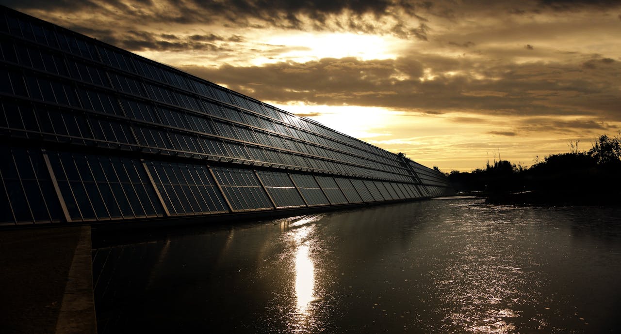 heros-img Silhouetted solar panels reflect sunset in tranquil waters, showcasing renewable energy.