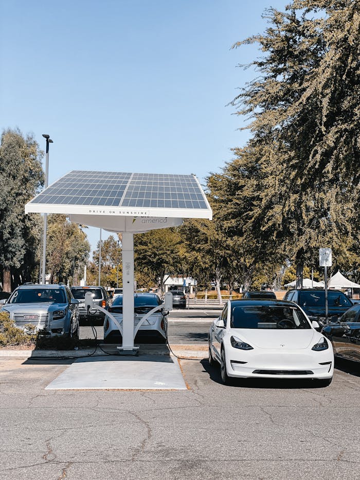 services-03 A white electric car charging under a solar panel in an urban setting, showcasing renewable energy use.